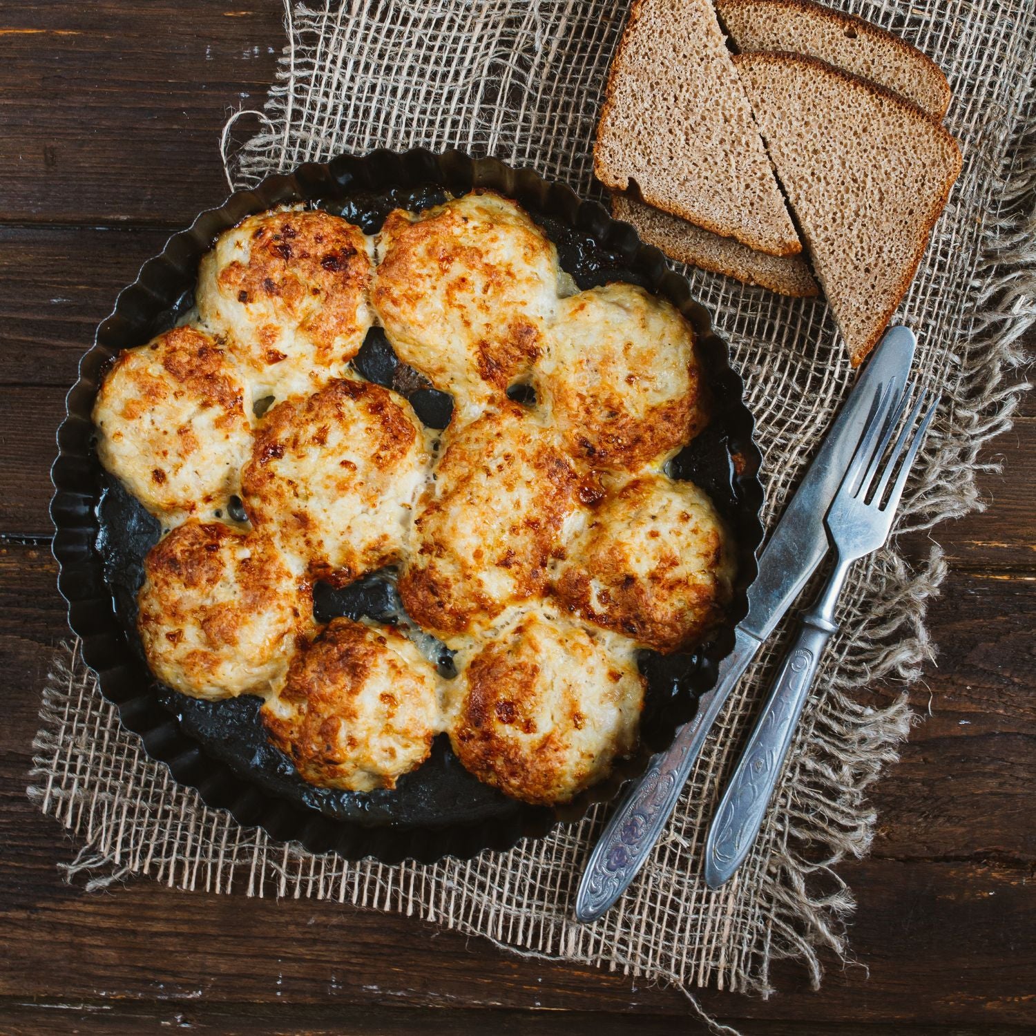 A close-up of a tray of baked meatballs, with a sprinkle of herbs and parmesan cheese on top